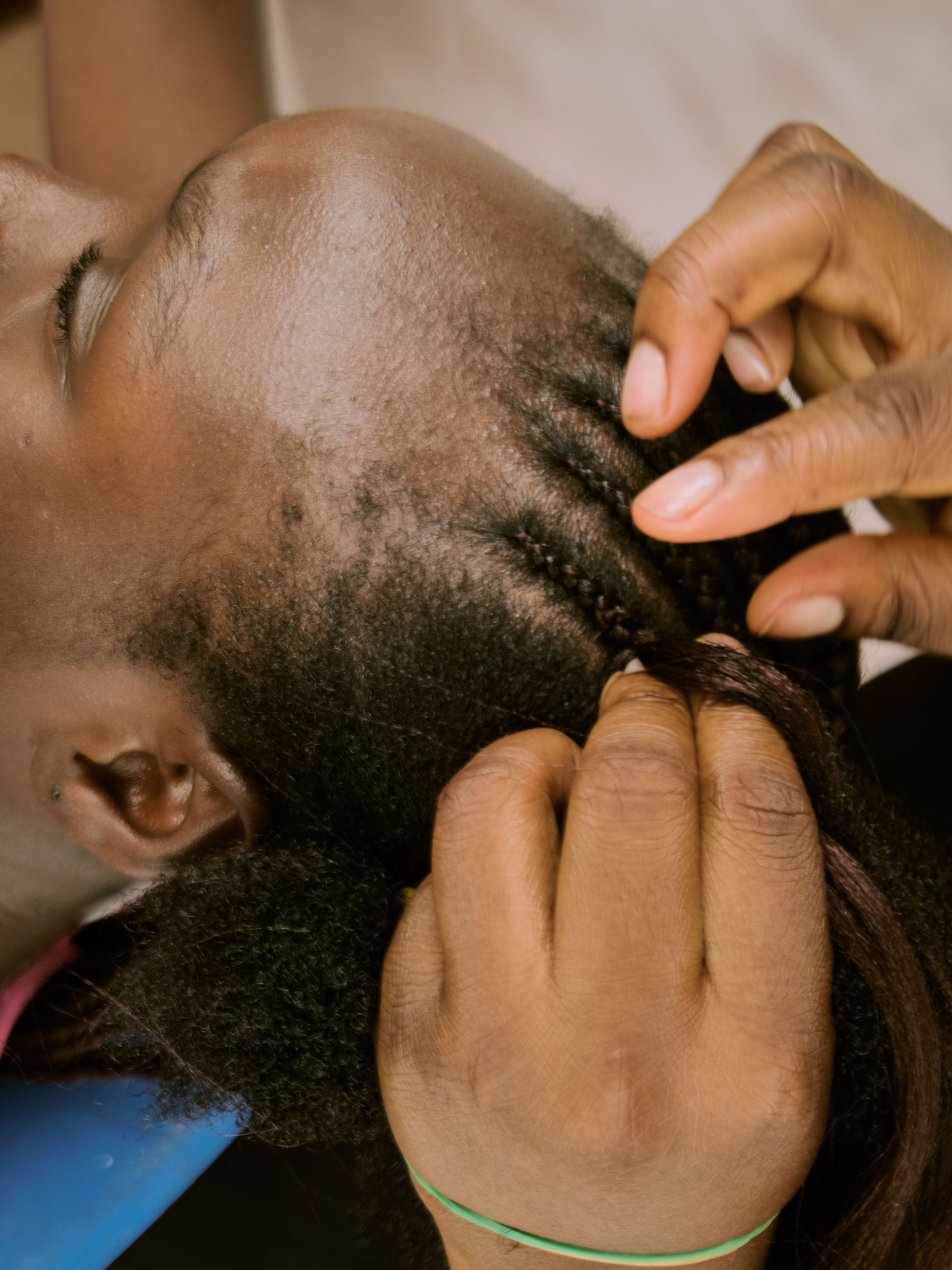 Gros plan de mains en train de tresser une chevelure afro, geste de pose et de tension sur le cuir chevelu