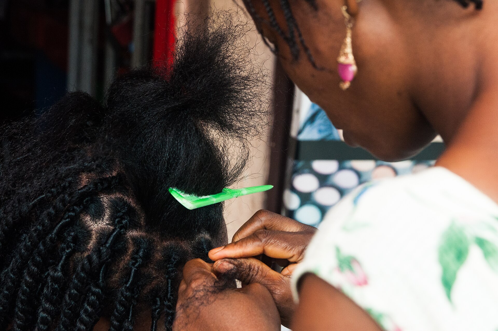 coiffeuse qui peigne et tresse les cheveux au niveau des tempes d'une cliente, dans un salon