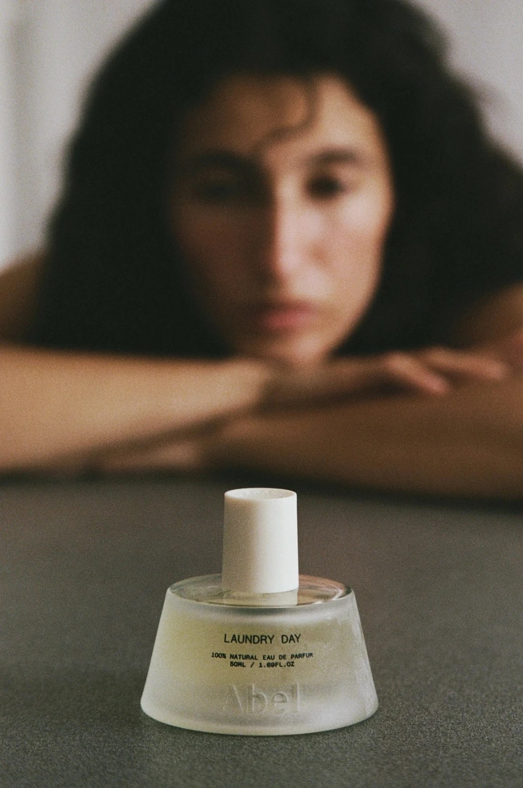 Flacon de parfum Abel Laundry Day au premier plan, femme accoudée floue derrière